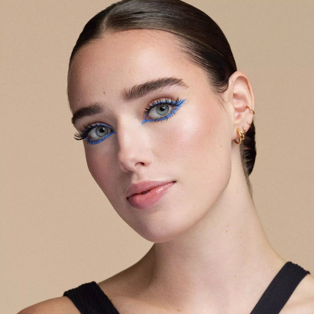 Porträt einer Frau mit blauer Eyeliner und falschen Wimpern. Sie lächelt.