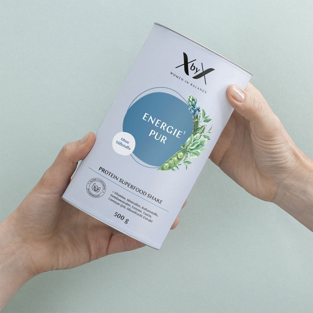 Hände halten Zylinderdose. Aufschrift: Energie Pur, Protein Superfood Shake. Dose mit blauem Kreis und Pflanzenmotiv.