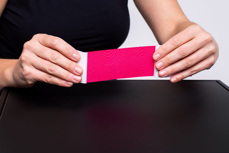 Rosa Kinesiotape, das von einer Person gehalten wird. Das Tape ist auf einer Rolle.