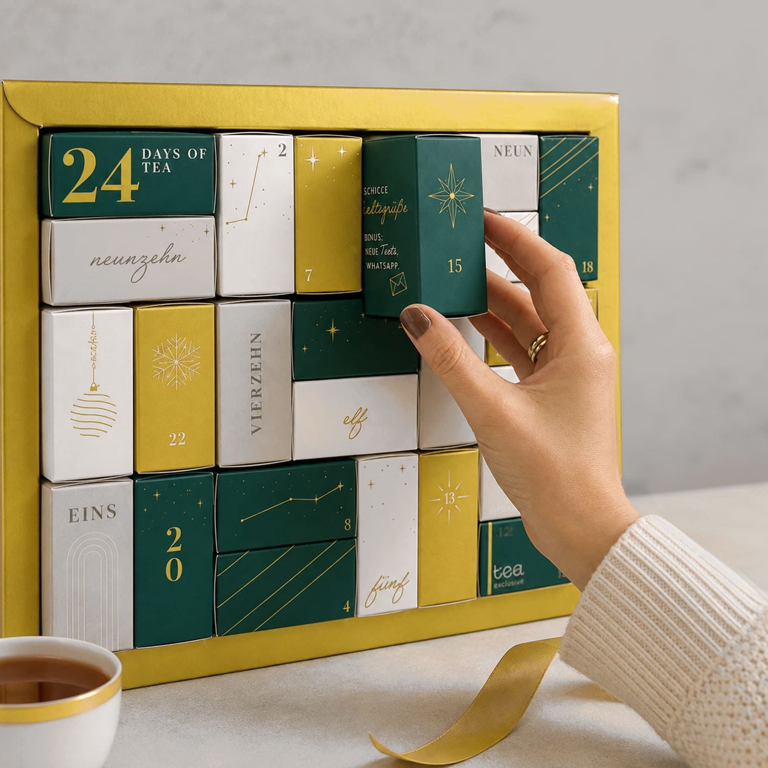 Hand nimmt eine grüne Schachtel aus einem goldenen Tee Adventskalender mit 24 Türchen.