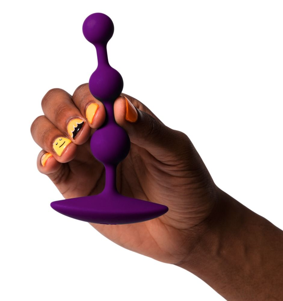 Lila Analperlen in einer Hand gehalten. Drei Kugeln und flacher Griff. Gelbe und orangefarbene Nagelkunst.