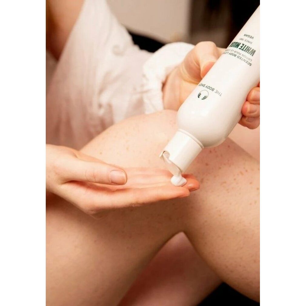 Person gibt Creme aus weißer Flasche mit Text White Musk auf die Hand. Bein im Hintergrund.