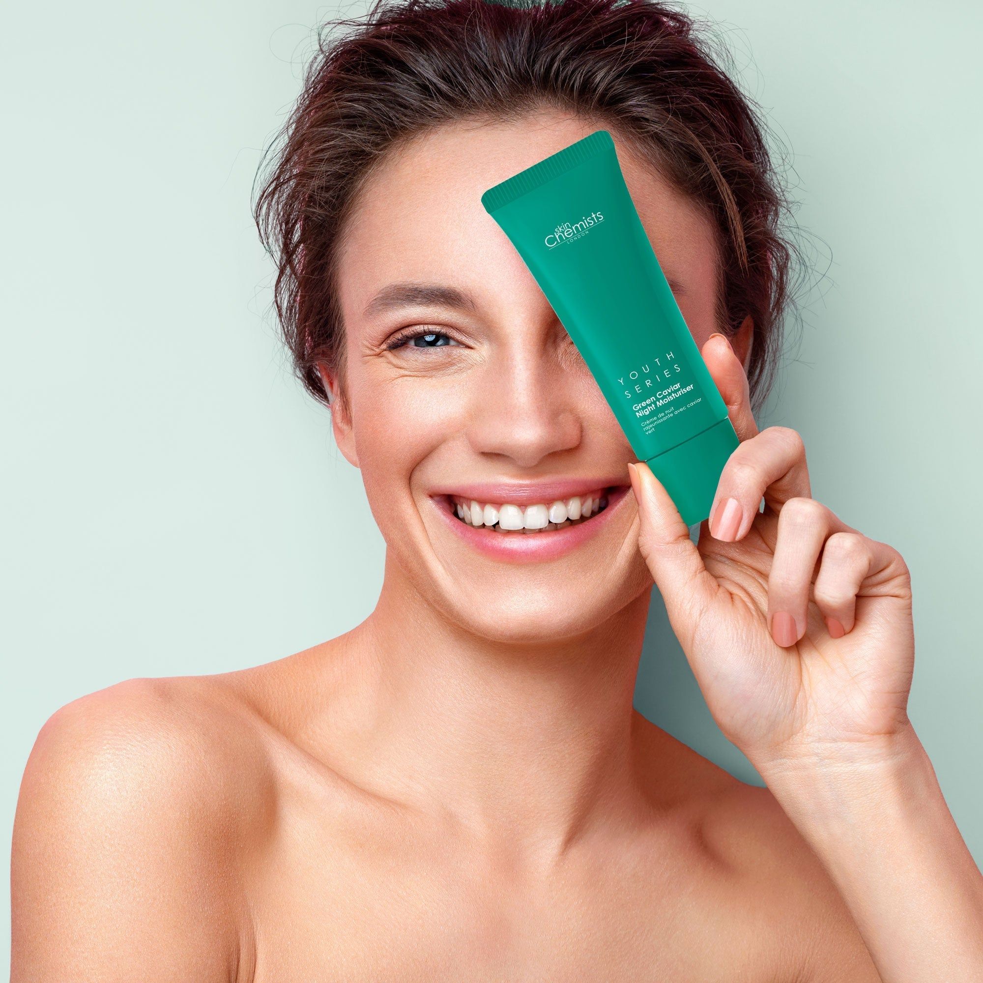 Frau hält grüne Tube vor dem Auge. Aufschrift: SkinChemists, Youth Series, Green Caviar Night Moisturiser.