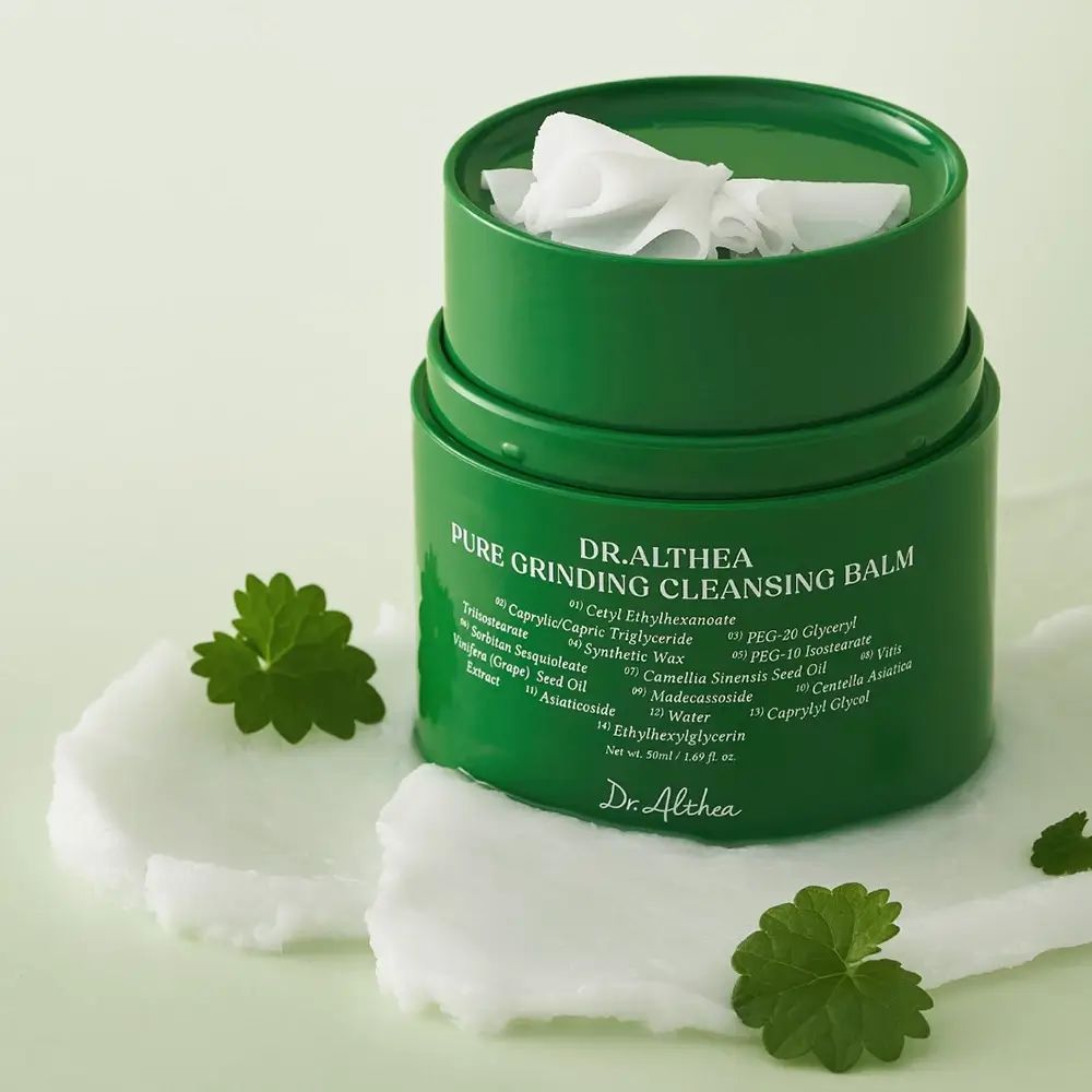 Grüner Behälter mit weißem Reinigungsbalsam. Aufschrift: Pure Grinding Cleansing Balm. Deckel mit weißen Tüchern.