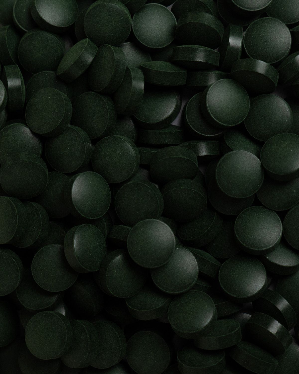 Nahaufnahme von vielen grünen, runden Tabletten. Die Tabletten sind flach und dicht gepackt.