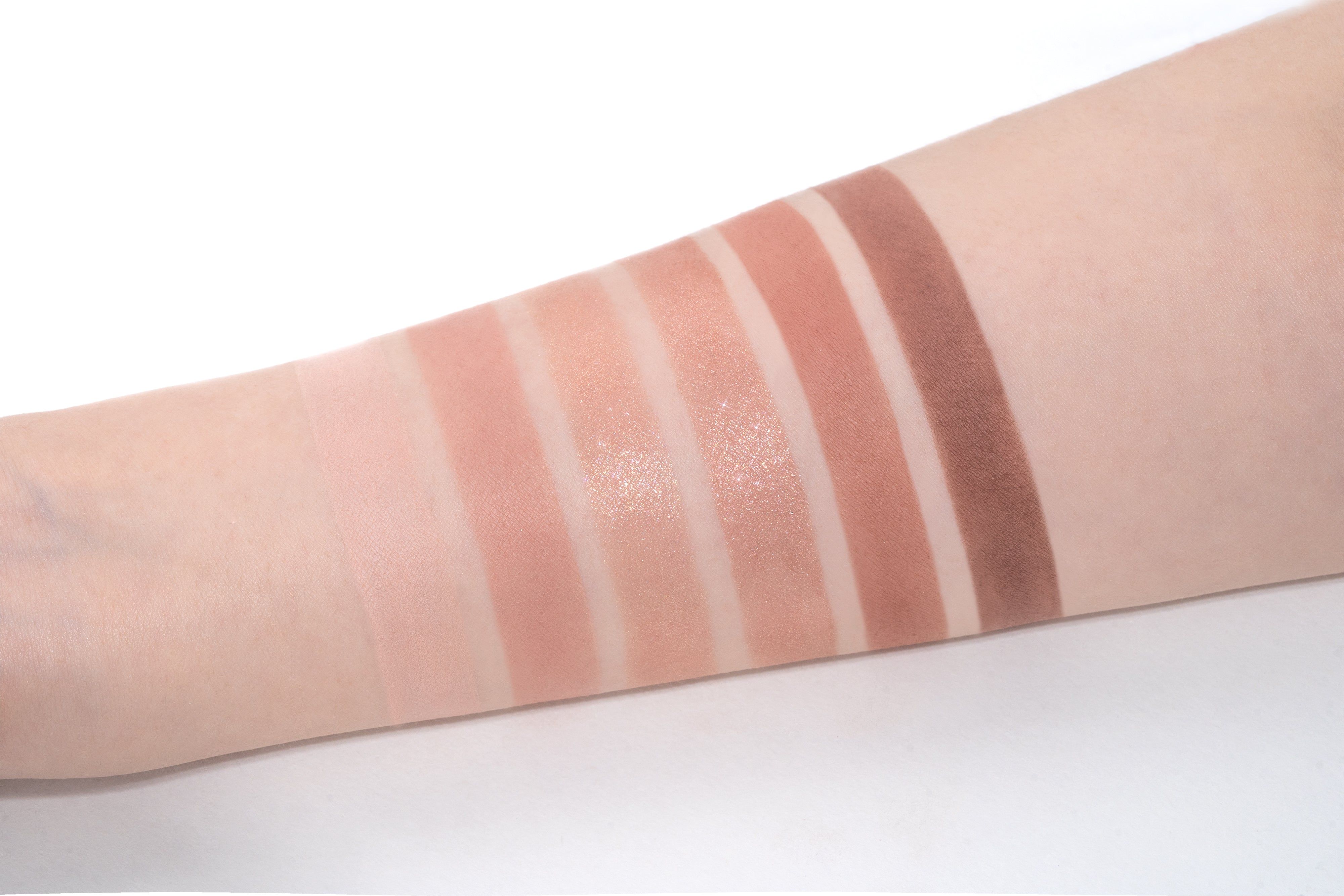 Arm mit sechs Lidschatten-Swatches in verschiedenen Brauntönen. Auf weißem Hintergrund.