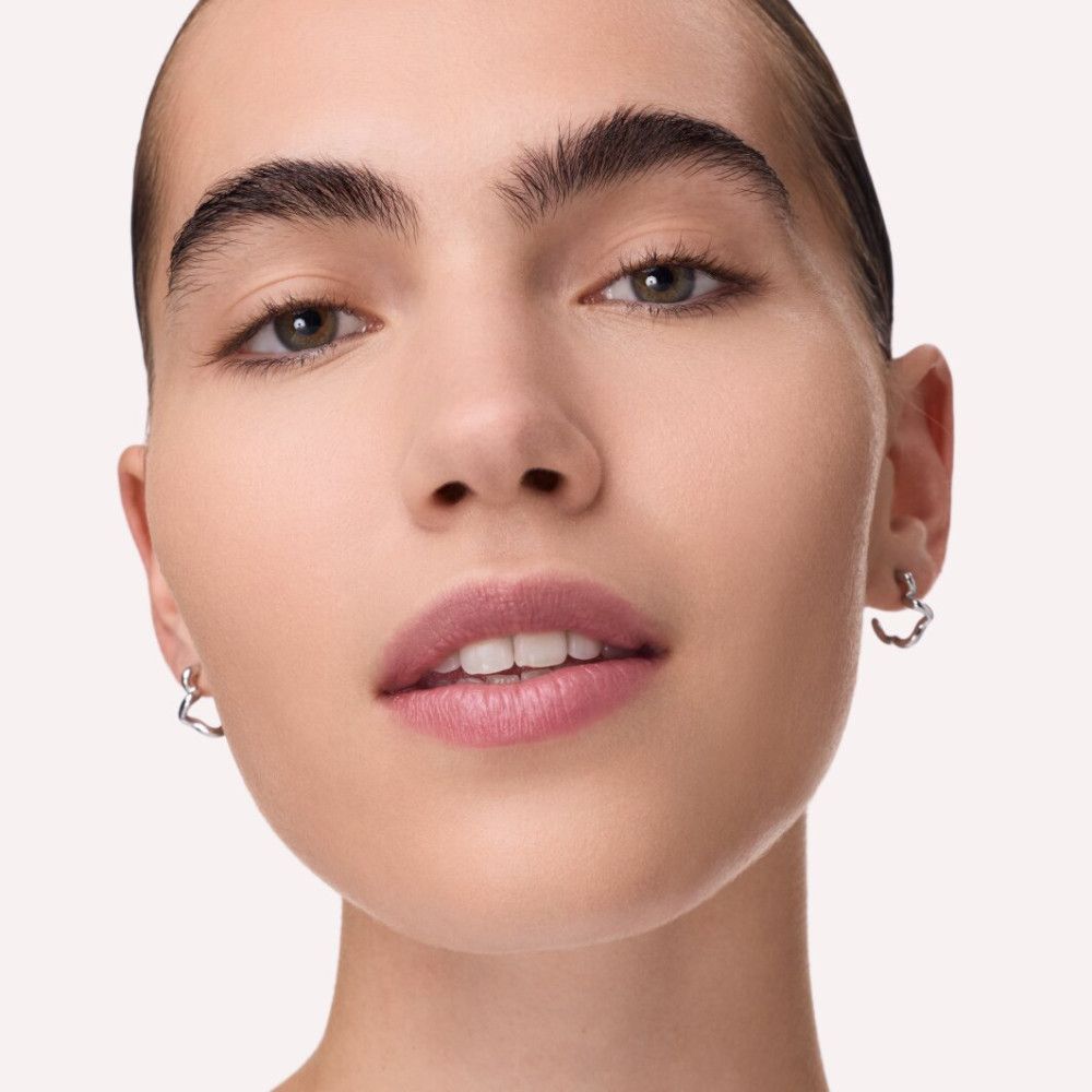 Nahaufnahme eines Gesichts. Frau mit dunklen Augenbrauen, rosa Lippen und silbernen Ohrringen.