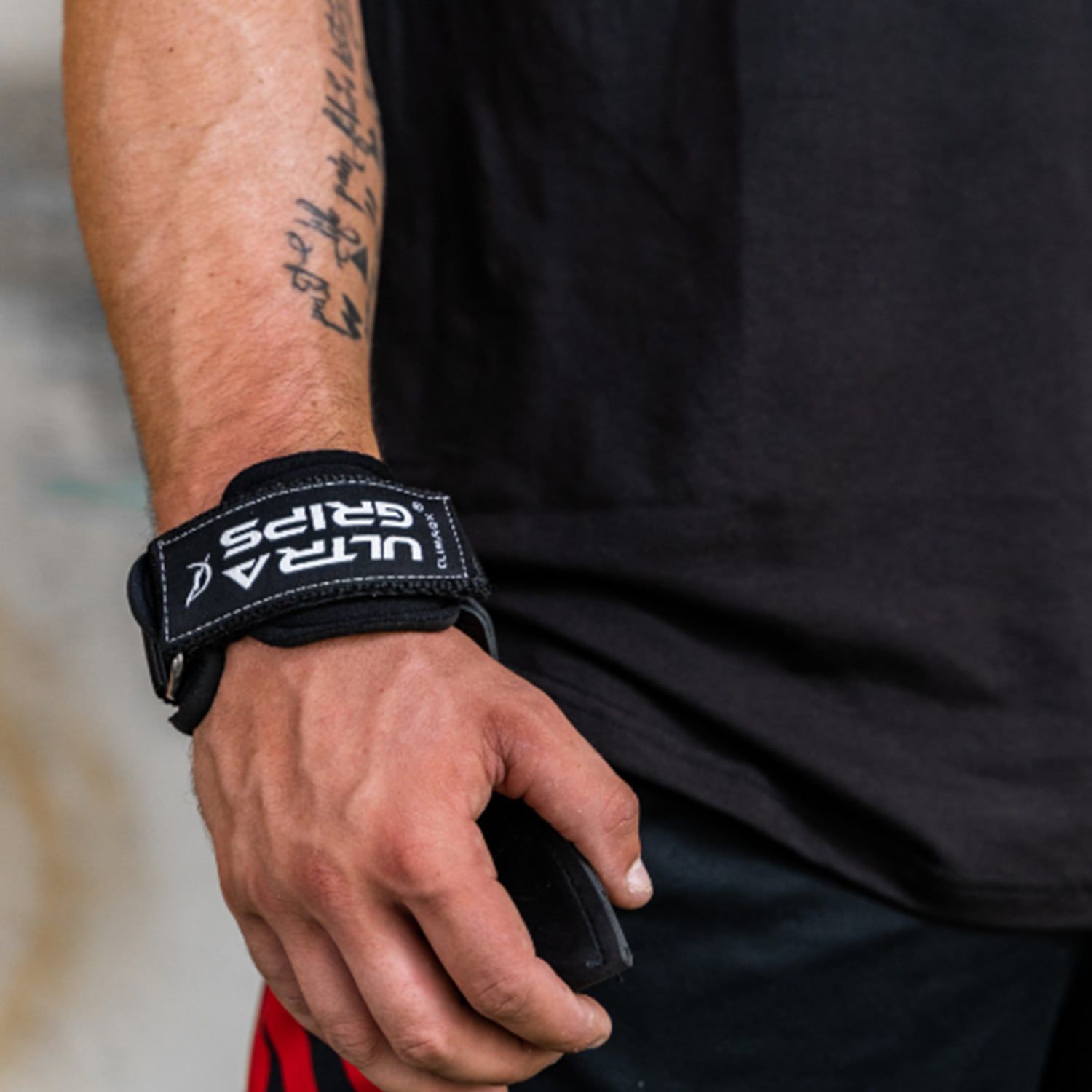 Nahaufnahme eines Handgelenks mit Ultra-Grip. Schwarzer Riemen mit "ULTRA GRIPS" Schriftzug.