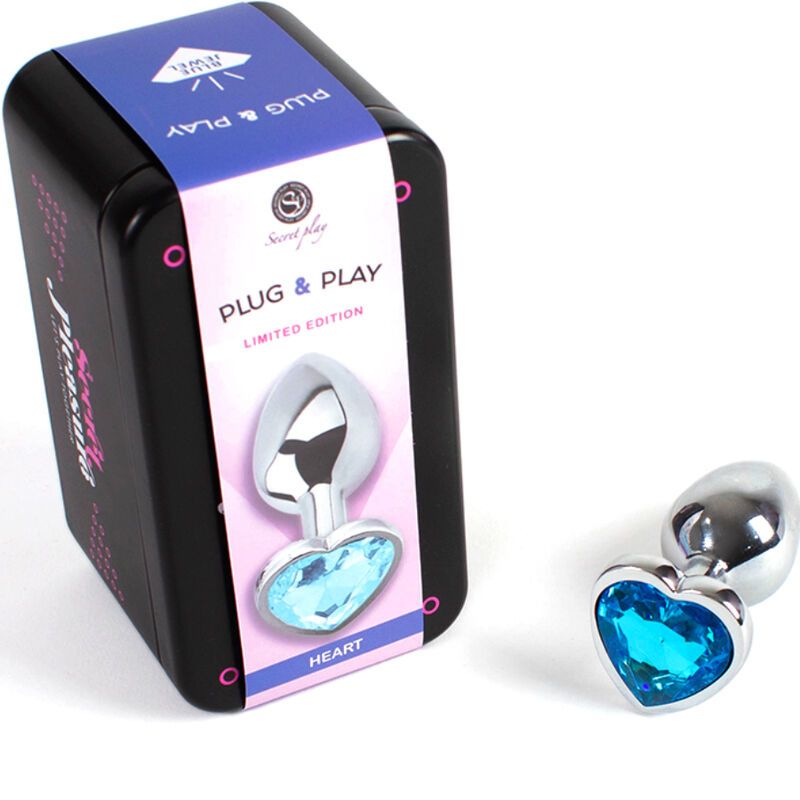 Metall-Butt Plug mit blauem Herz-Design. Neben schwarzer Dose mit Aufschrift 'Plug & Play' und 'Secret Play'.