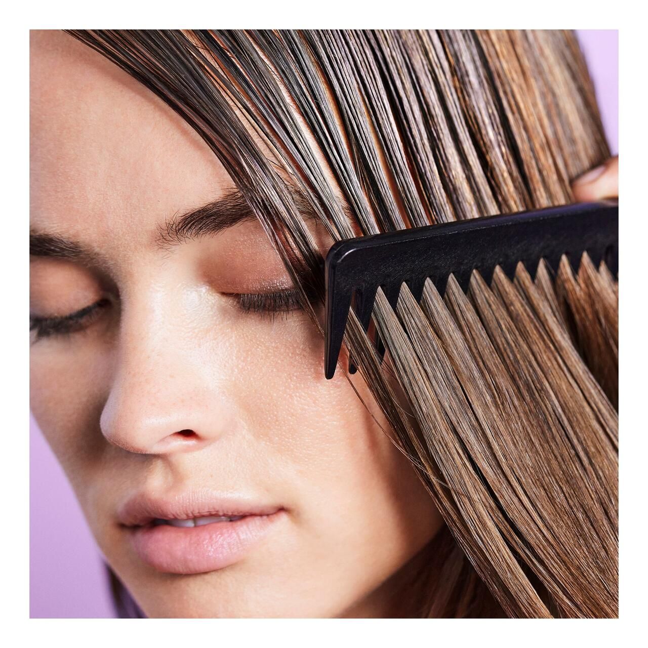 Frau kämmt ihr nasses Haar. Schwarzer Kamm. Hintergrund lila.