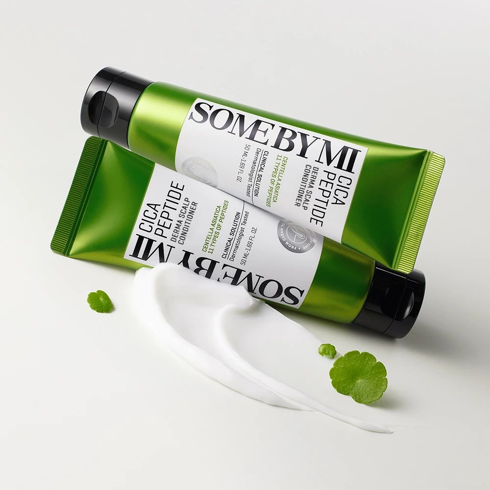 Zwei grüne Tuben SOME BY MI Cica Peptide. Weiße Creme daneben. Grüne Blätter. Helle Oberfläche.