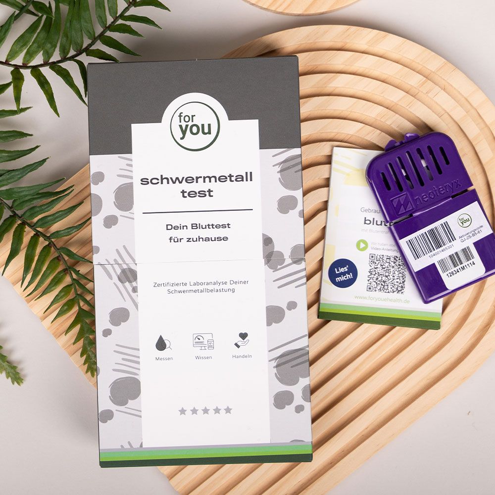 Verpackung des 'for you schwermetall test' auf einem Holzteller, daneben ein kleiner Beipackzettel.