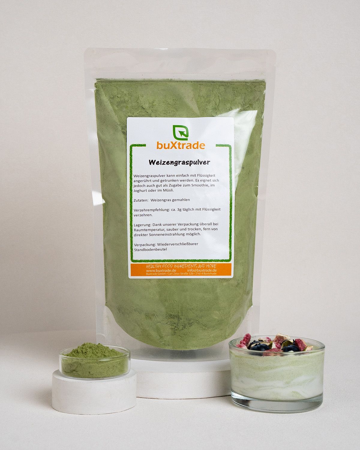 Ein Beutel buxtrade Weizengraspulver neben einer Schale mit einem grünen Smoothie und einem Löffel Pulver.