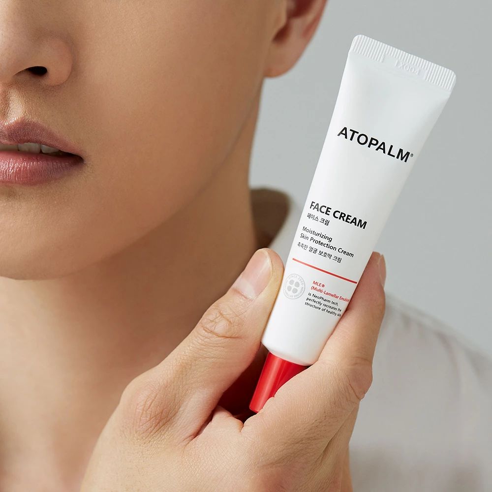 Weiße Tube mit rotem Verschluss, gehalten von einer Person. Aufschrift: ATOPALM, FACE CREAM. Nahaufnahme.