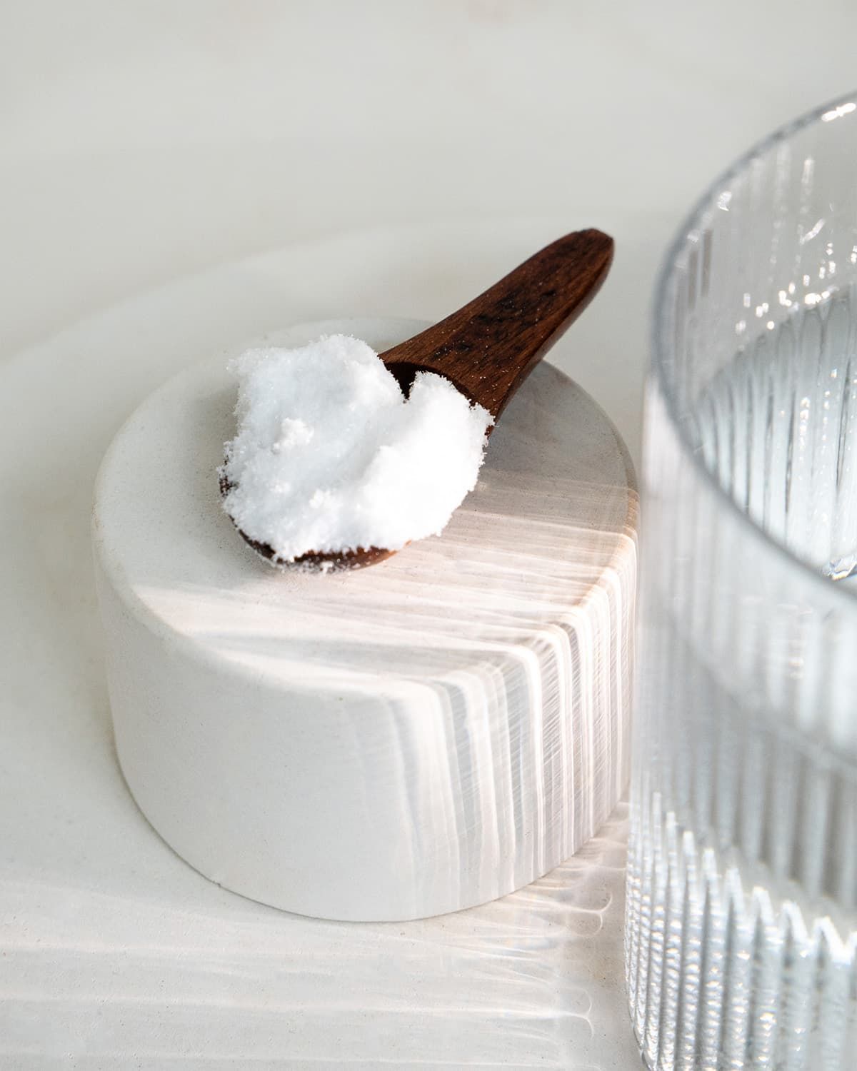Ein Holzlöffel mit weißem L-Ornithin Pulver auf einem weißen Zylinder, daneben ein Glas Wasser.
