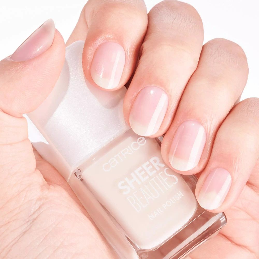 Hand mit lackierten Nägeln und Nagellackflasche. Aufschrift: CATRICE SHEER BEAUTIES NAIL POLISH.
