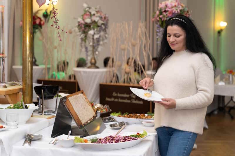 Frau am Buffet, nimmt Honig aus einer Wabe. Die Wabe ist in einem Holzrahmen. Auf dem Tisch sind Speisen und Dekorationen.