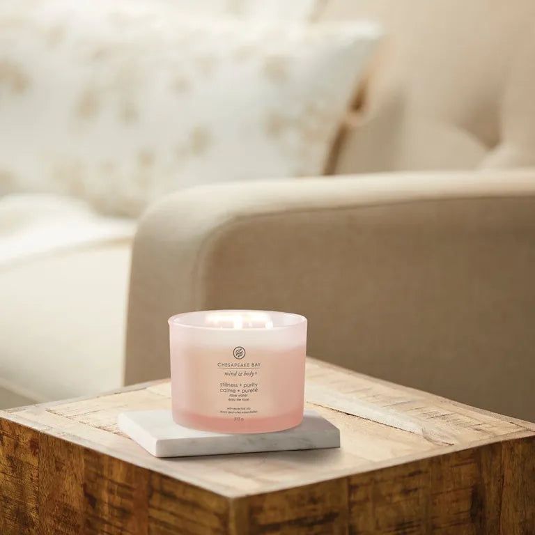 Rosafarbene Kerze auf einem Tisch. Aufschrift 'Chesapeake Bay'. Text: 'stillness + purity', 'rose water'. 3 Dochte.