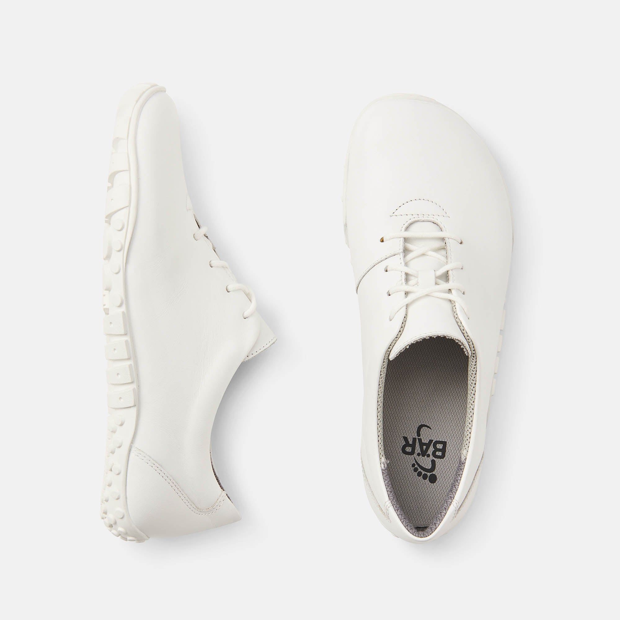 Zwei weiße Schuhe, Draufsicht. Schnürsenkel, flache Sohle. Innensohle mit Logo. Breite Passform.