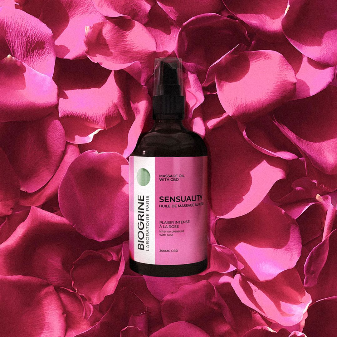 Bruine fles massageolie, omringd door roze rozenblaadjes. Opschrift: SENSUALITY, BIOGRINE.