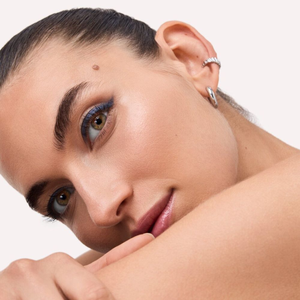 Nahaufnahme eines Gesichts mit blauem Eyeliner. Die Person hat braune Augen und einen Ohrring.