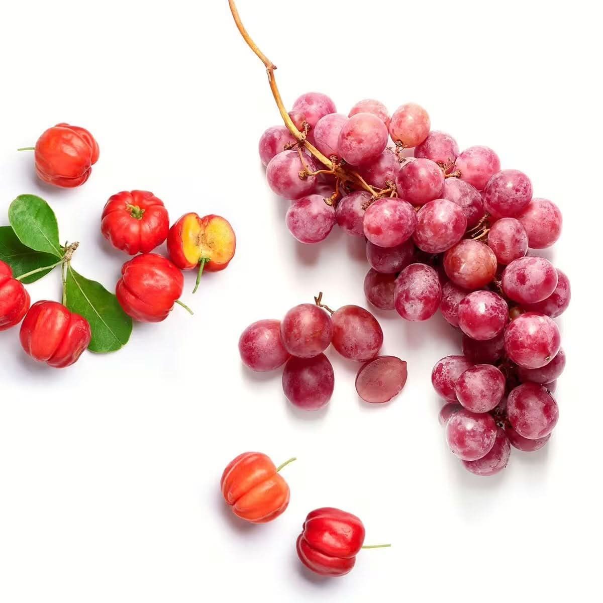 Frische rote Acerolakirschen und eine Traube auf weißem Hintergrund.