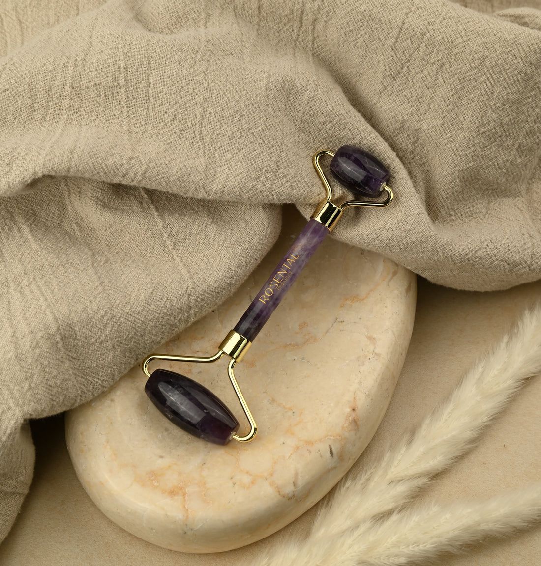 Amethyst Roller auf einem Stein platziert, umgeben von Stoff und Trockenblumen.