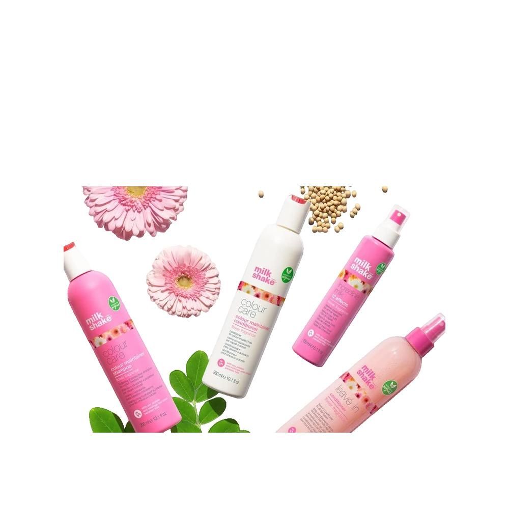 Vier Milk Shake Haarpflegeflaschen in Rosa und Weiß, umgeben von rosa Gerbera-Blüten und grünen Blättern.