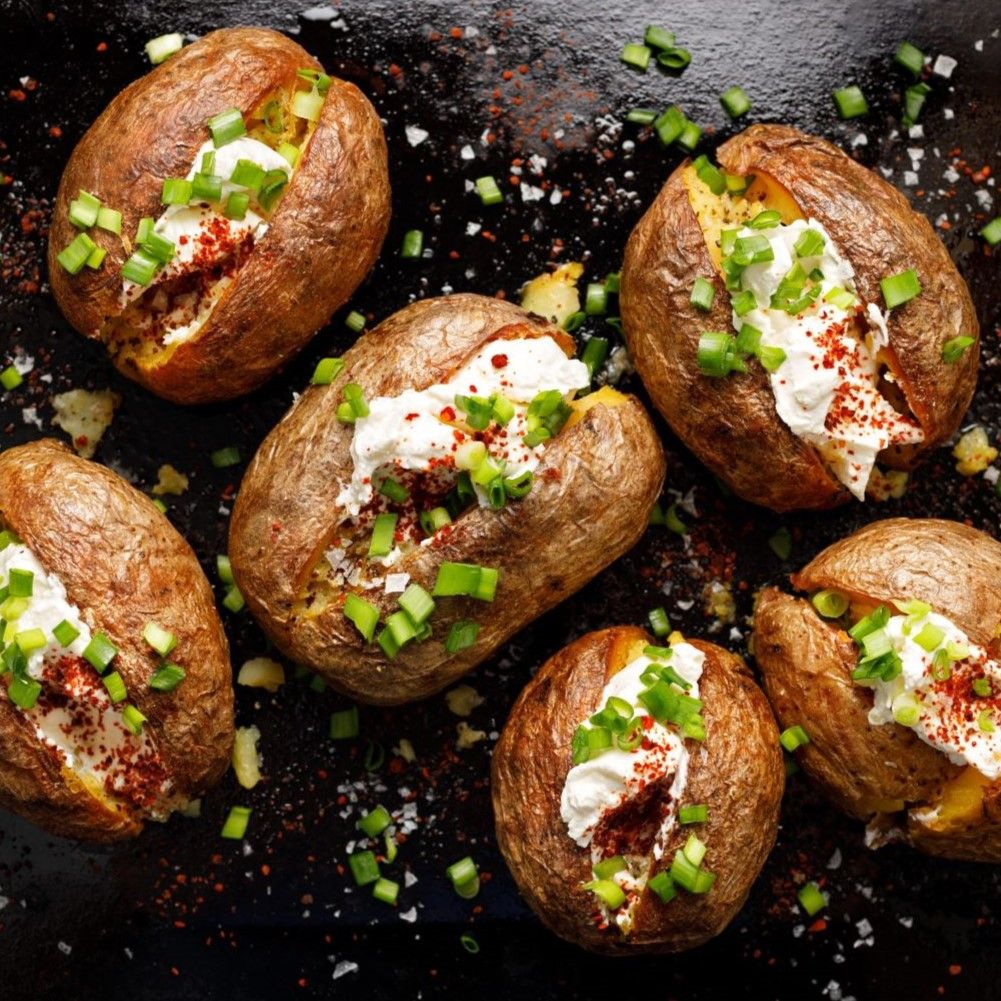 Sechs gebackene Kartoffeln mit Füllung aus Creme, Schnittlauch und Paprikaflocken. Auf schwarzem Untergrund.