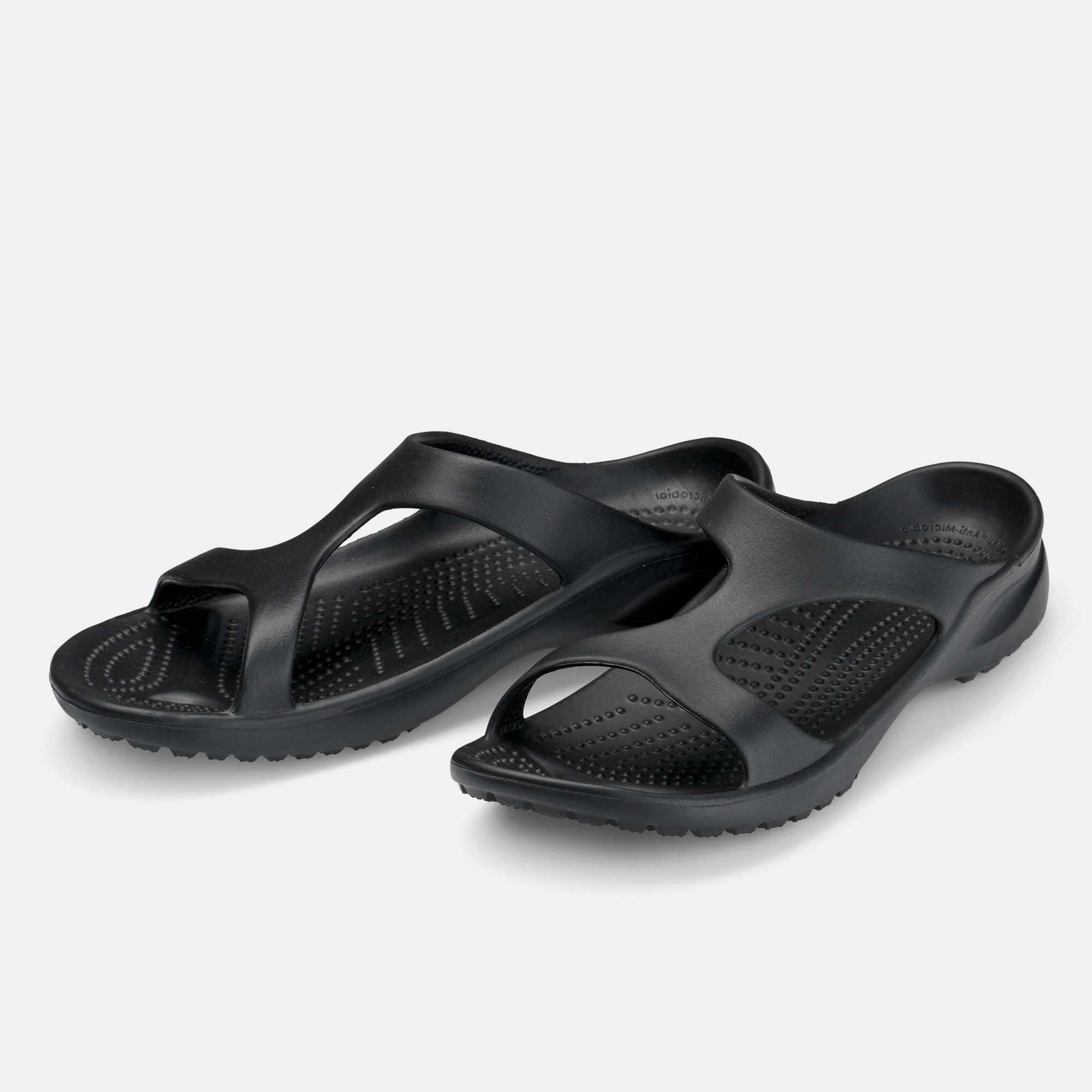 Schwarze Pantoletten. Breite Passform. Offene Zehen. Geformte Sohle. Zwei Schuhe nebeneinander.
