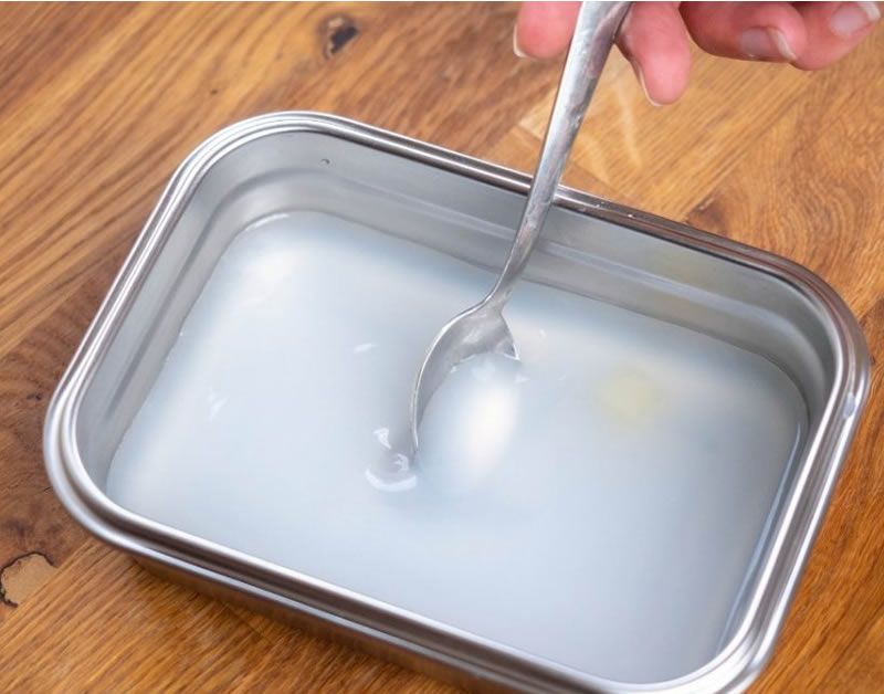 Löffel rührt in einer Flüssigkeit in einem Behälter. Flüssigkeit milchig. Behälter aus Metall.