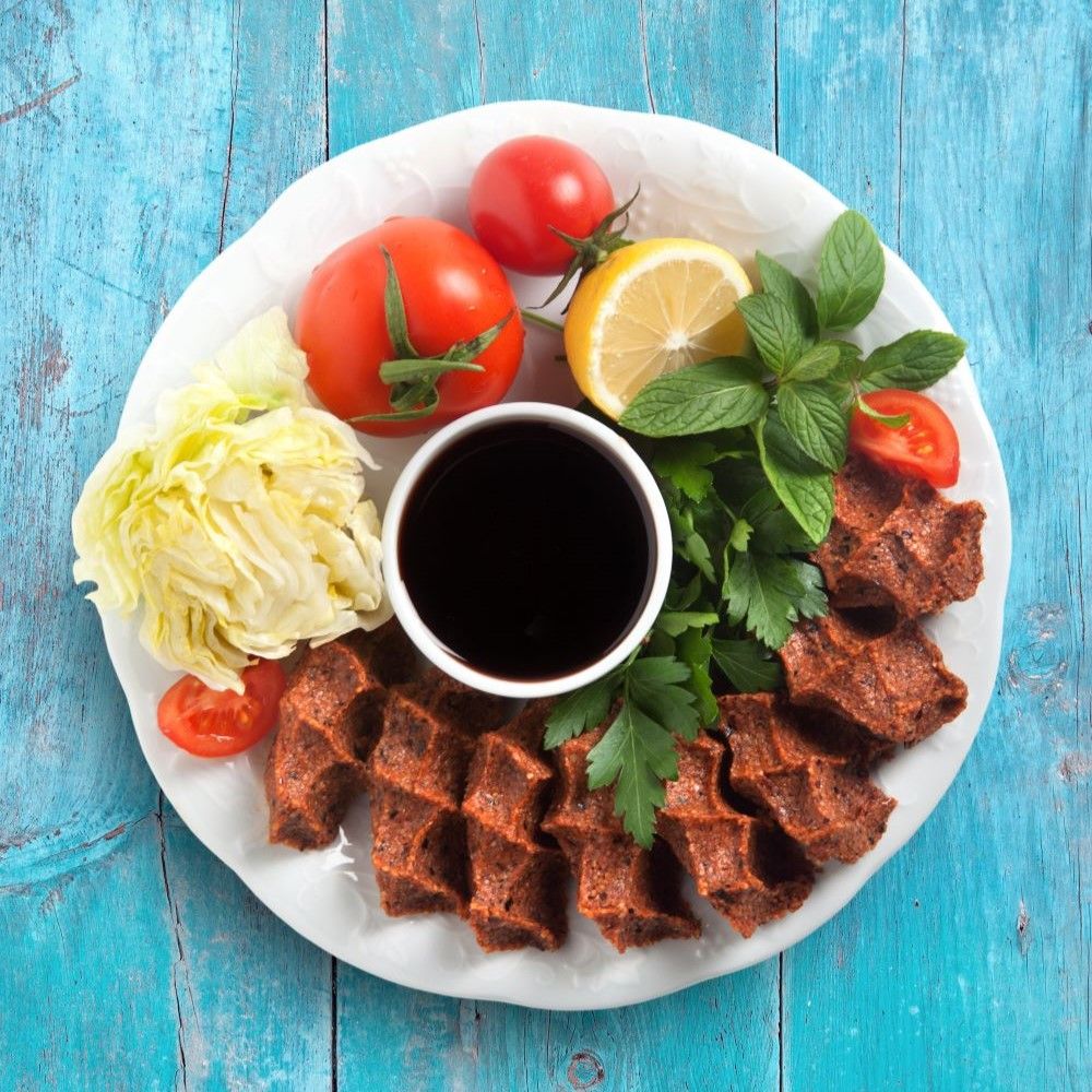 Teller mit Köfte, Tomaten, Zitrone, Salat und Sauce. Auf blauem Holzhintergrund.