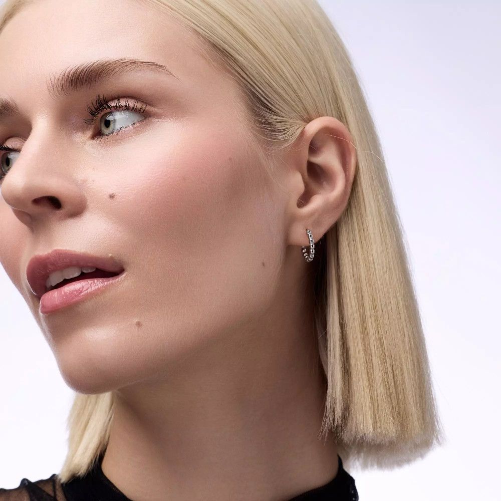 Nahaufnahme einer Frau mit blonden Haaren. Sie trägt Ohrringe und schaut zur Seite.