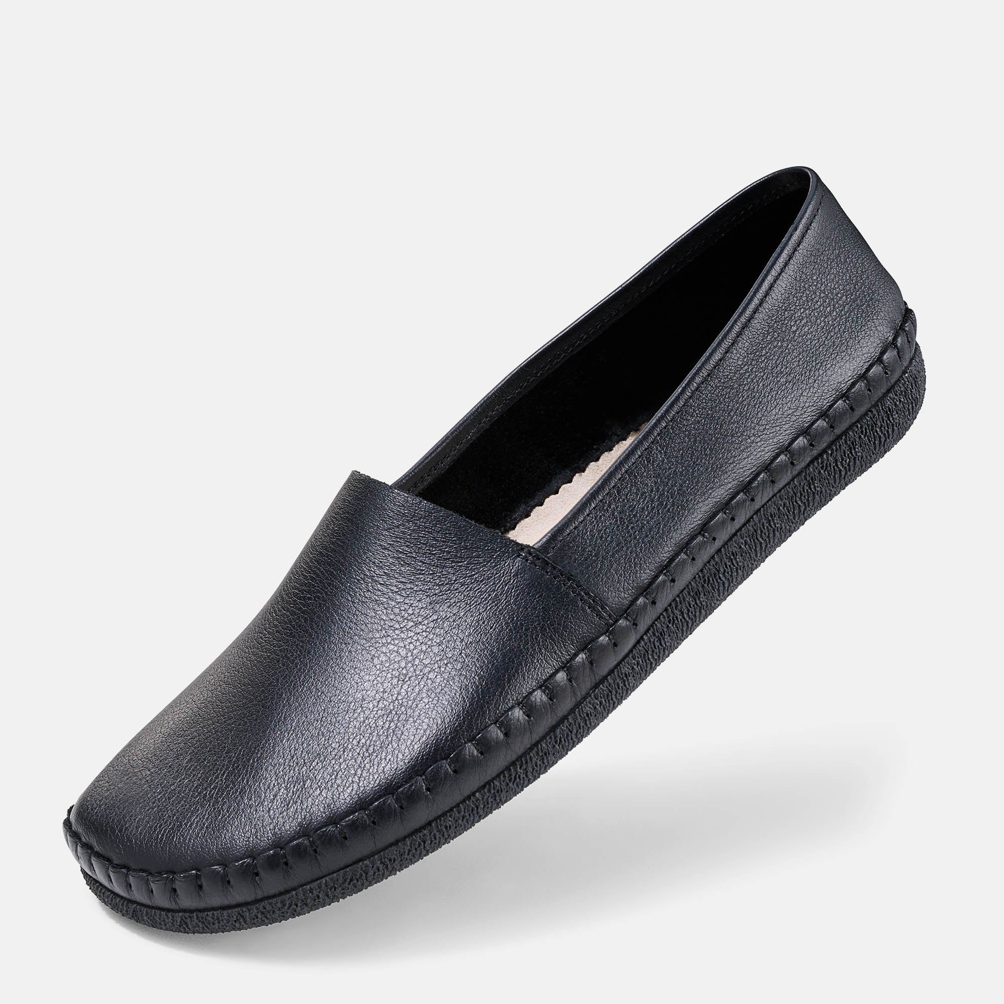 Schwarzer Unisex-Slipper. Glattes Leder, flache Sohle, quadratische Zehenpartie. Sichtbare Ziernähte. Schuh leicht schräg.