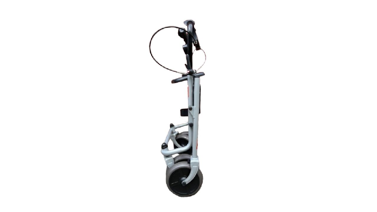 Opgevouwen rollator van de zijkant. Grijs metalen frame, zwarte wielen. Remmen en handgrepen zichtbaar.
