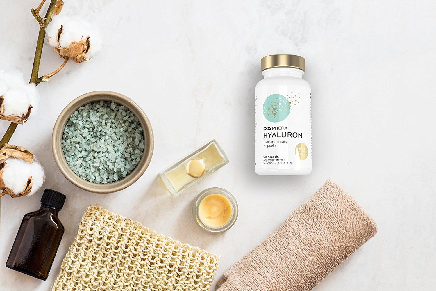 Cosphera Hyaluronsäure Kapseln in weißer Flasche mit goldenem Deckel, neben Wellness-Produkten.