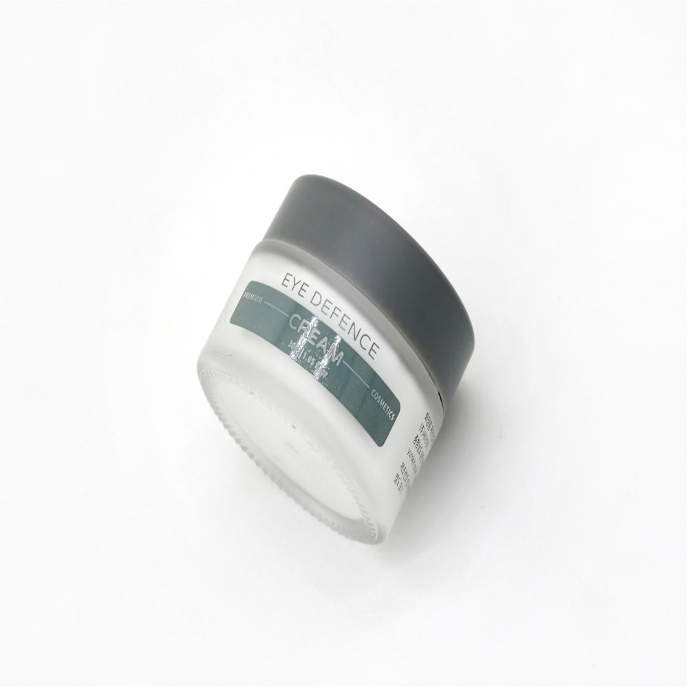Schräg gestelltes Creme-Glas mit grauem Deckel. Aufschrift: Eye Defence Cream.