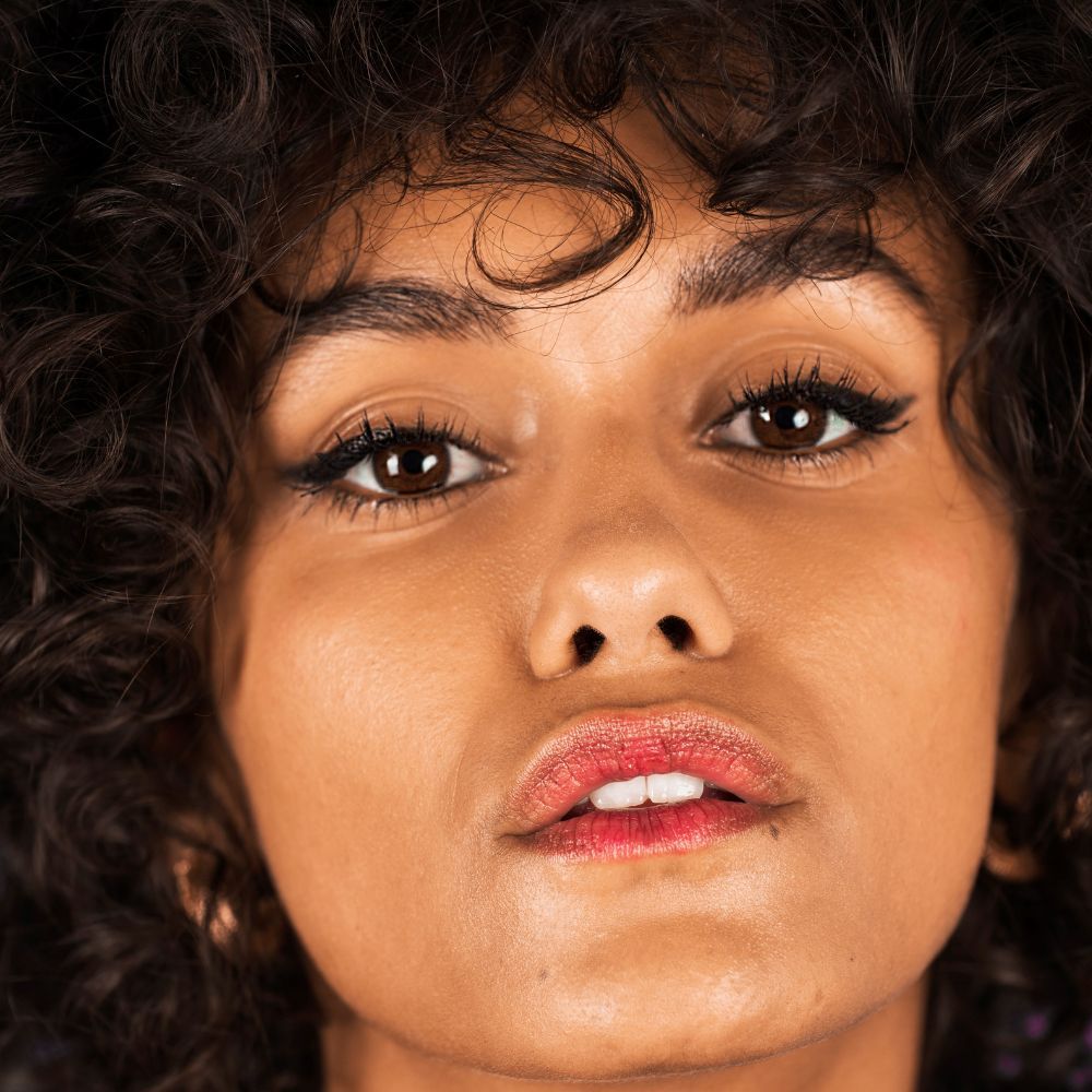Porträt einer Frau mit dunkler Haut und Locken. Schwarzer Eyeliner auf den Augenlidern. Roter Lippenstift.