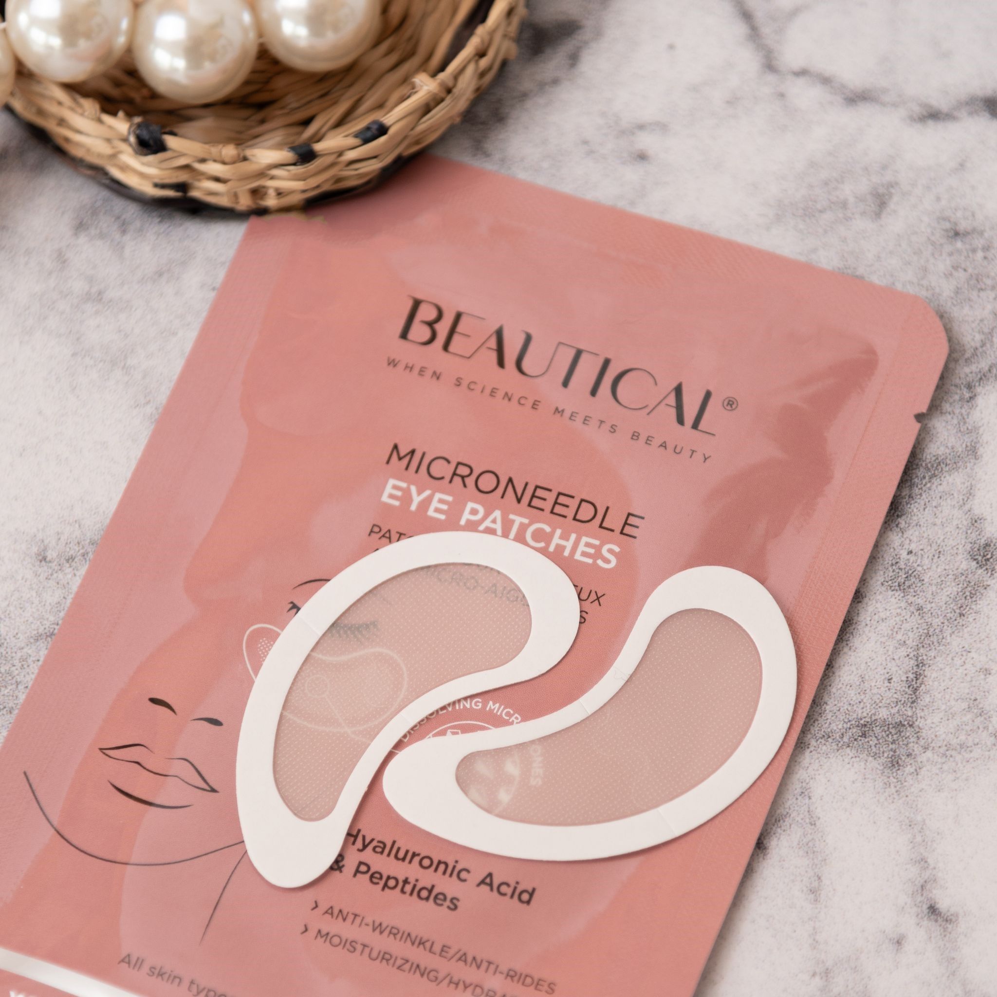 Rosa Verpackung mit BEAUTICAL Mikronadel-Augenpads und zwei Pads. Auf einer Oberfläche mit Perlen.