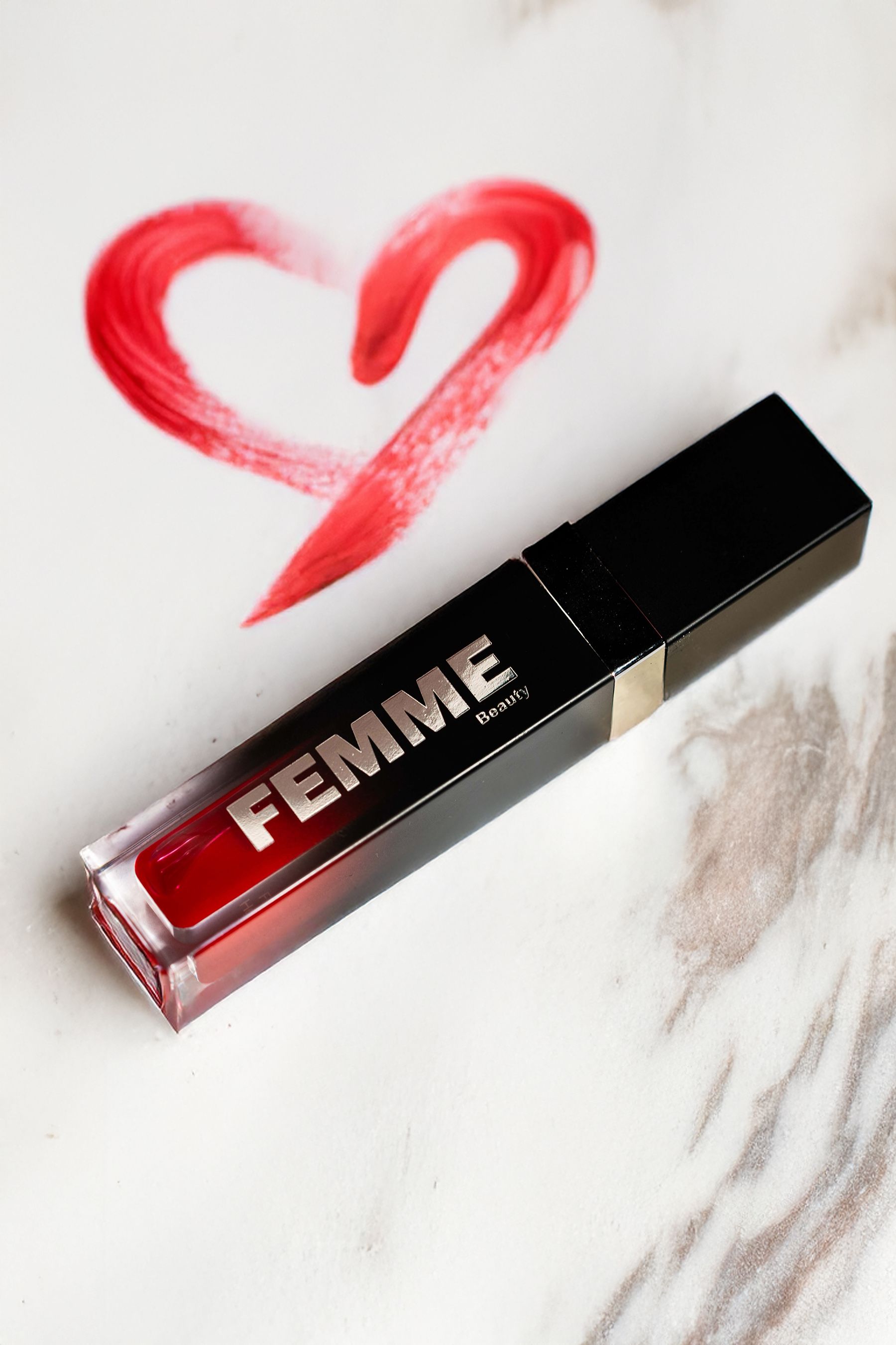 FEMME Beauty Lip Oil in roter Farbe, in durchsichtiger Hülle mit schwarzem Deckel. Roter Herz-Pinselstrich daneben.