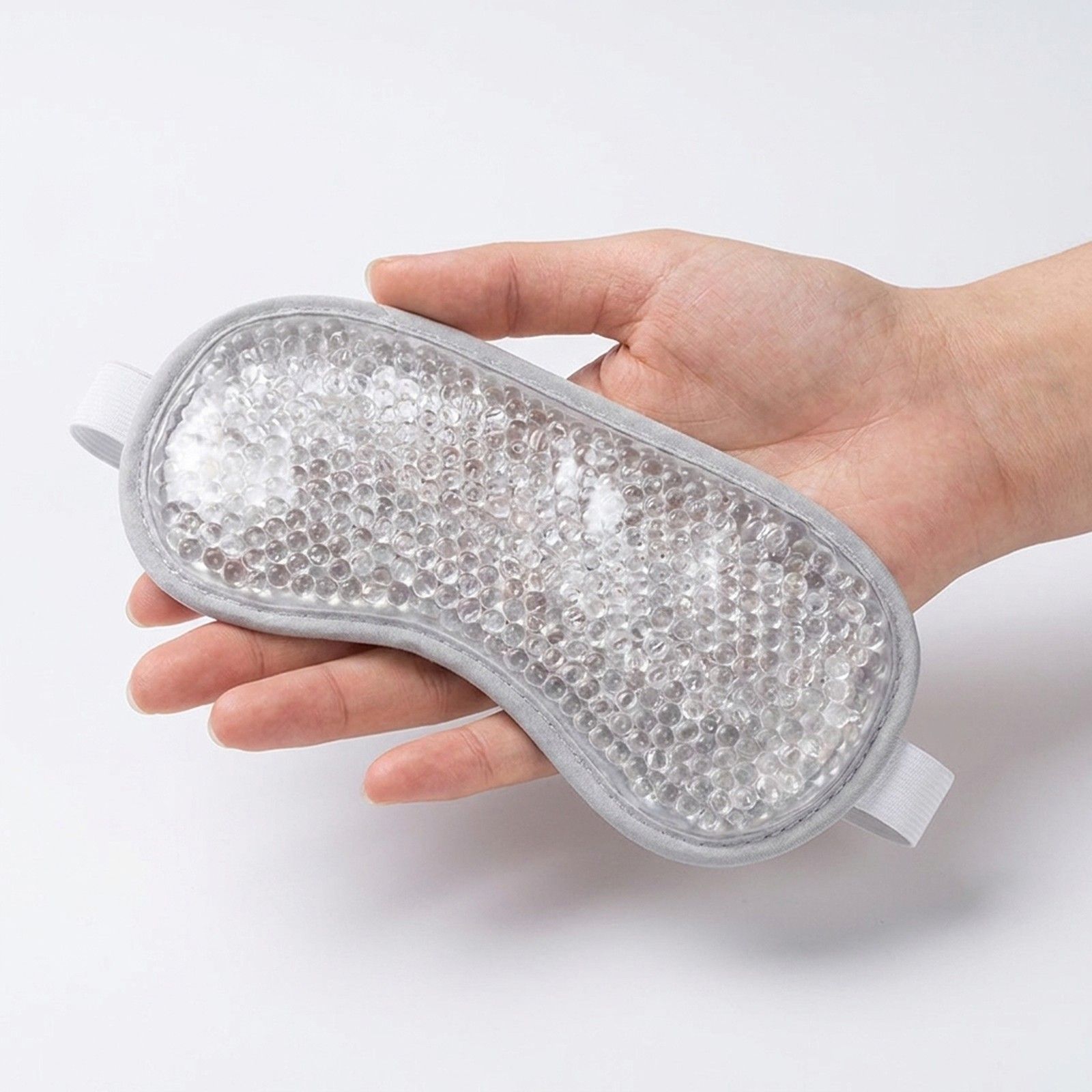 Hand hält eine graue Augenmaske mit Kügelchenfüllung.