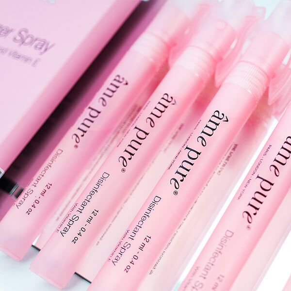 Close-up van roze sprays. Opschrift: âme pure Disinfectant Spray, 12 ml - 0.4 oz, with Vitamin E.