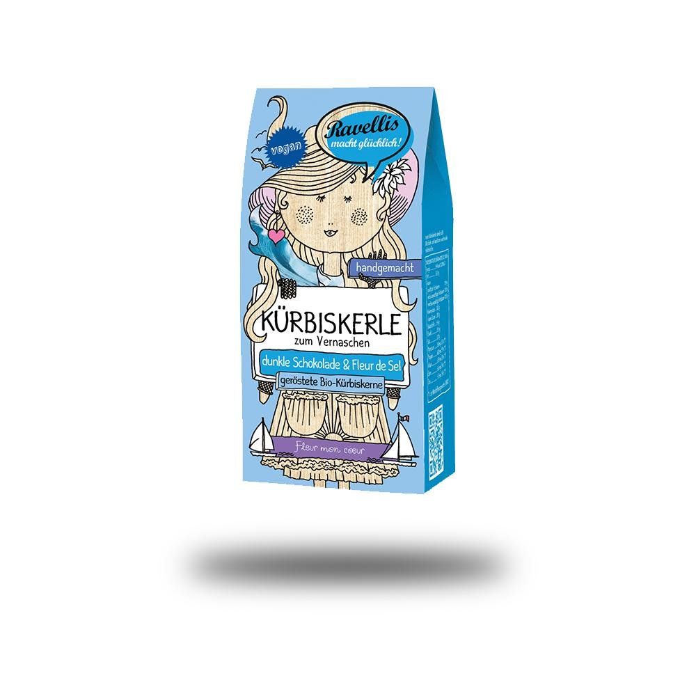 Blau-weiß verpackte Kürbiskerne. Aufdruck: K
ürbiskerle, dunkle Schokolade & Fleur de Sel, vegan. Illustration einer Frau.