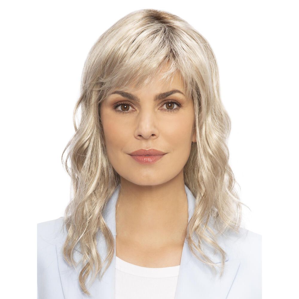 Perücke Kiky von trendhair. Blond, gewellt, mit Pony. Frau trägt hellblaues Jackett. Frontale Ansicht.