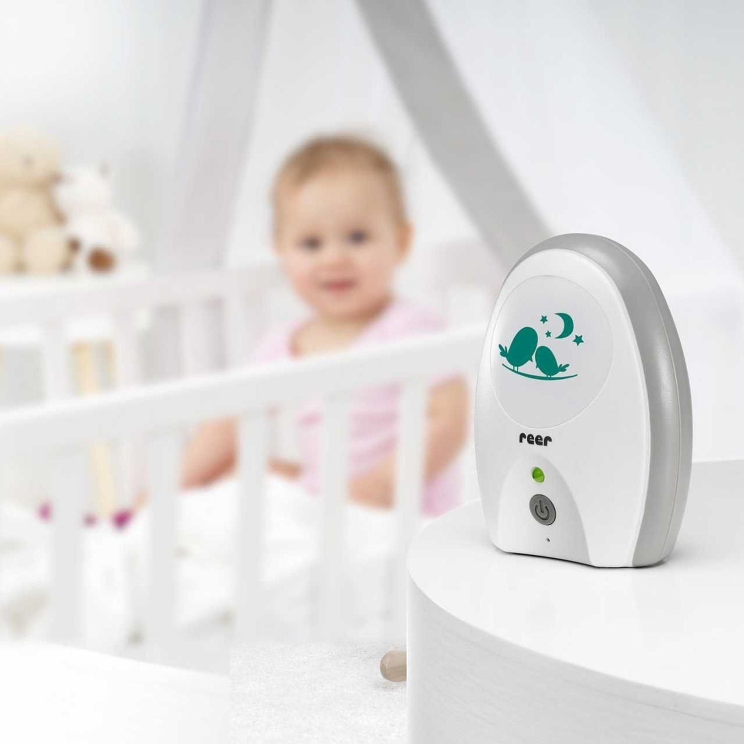Ein Babyfon steht auf einem Tisch vor einem Babybett. Ein Baby schläft im Bett.