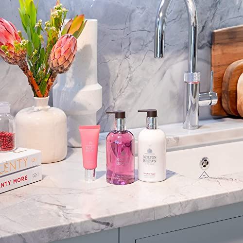 Szene mit Molton Brown Produkten. Handseife, Handlotion, Creme. Auf einer Theke. Blumenarrangements. Wasserhahn im Hintergrund.