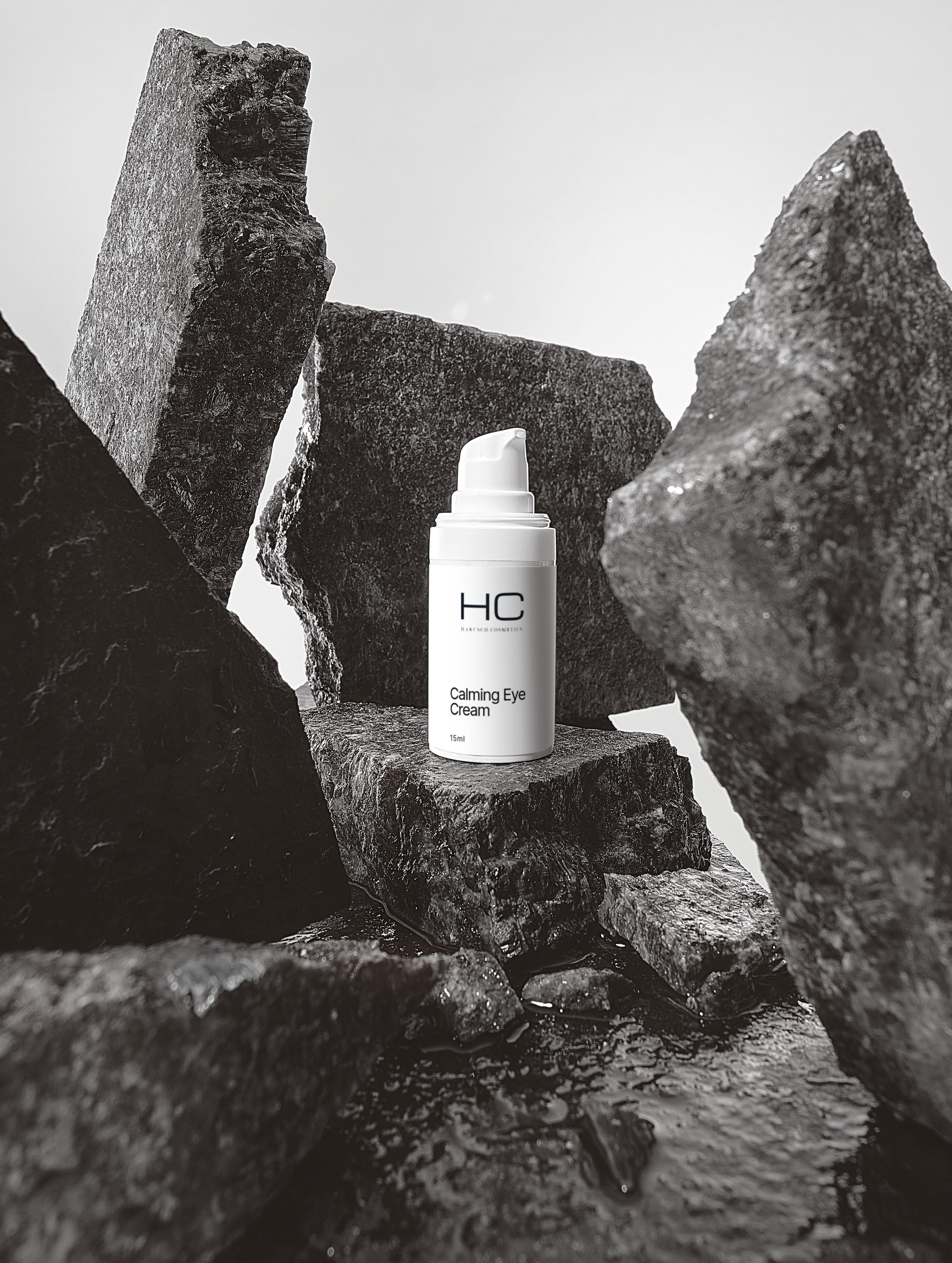 Weiße Flasche "HC Calming Eye Cream" auf Steinen. Schwarz-Weiß-Foto.