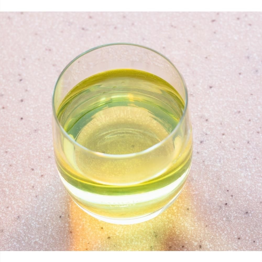 Glas mit gelblicher Flüssigkeit. Das Glas ist rund und steht auf einer hellen Oberfläche. Die Flüssigkeit ist durchsichtig.