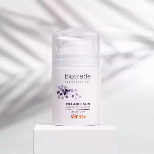 Weiße Flasche mit Pumpverschluss. Aufschrift: Biotrade, Melabel Sun Sonnenschutzcreme SPF 50+. Steht auf weißem Podest.