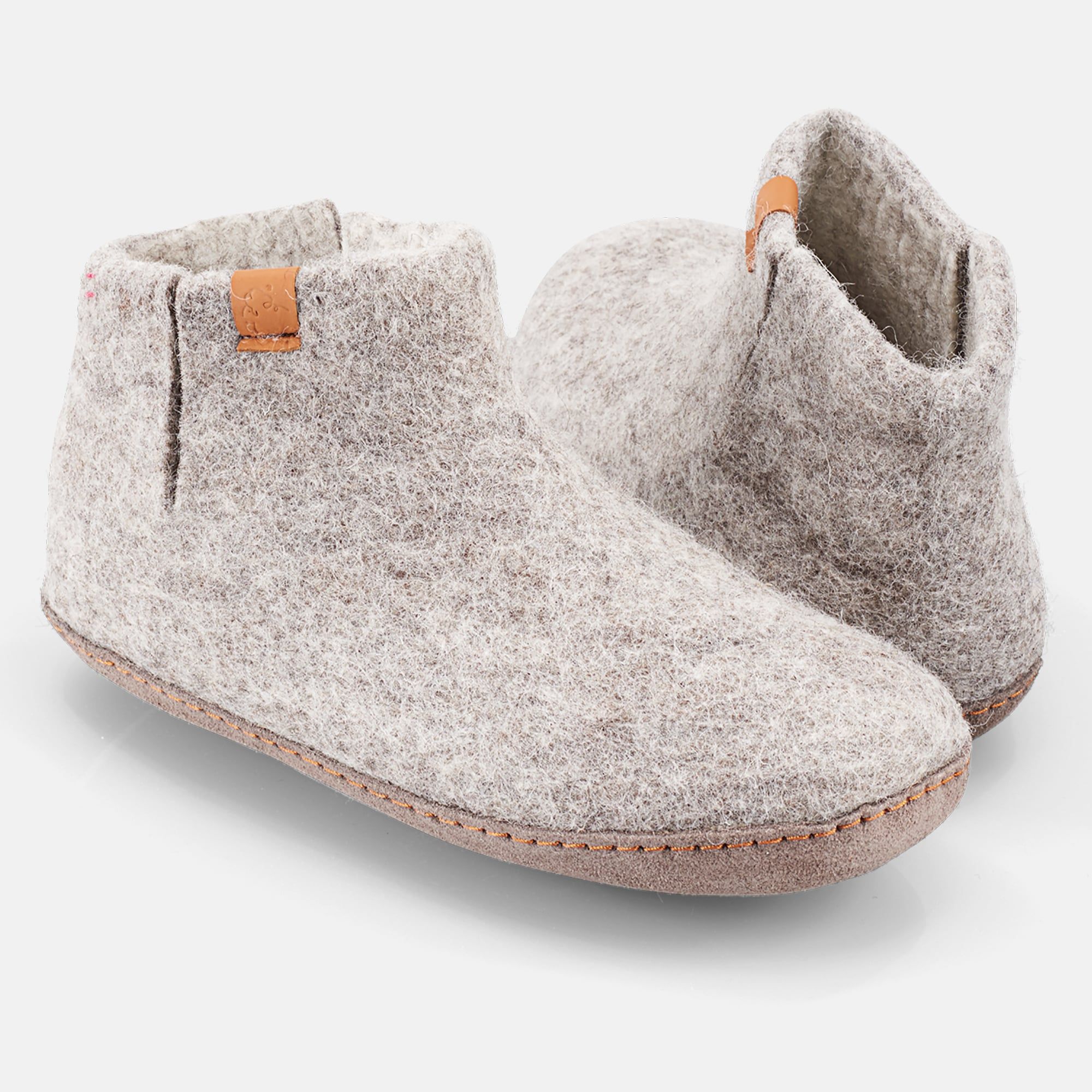 Graue Filz-Hausschuhe, breite Form, mit braunen Lederdetails. Seitliche Ansicht, zwei Schuhe nebeneinander.